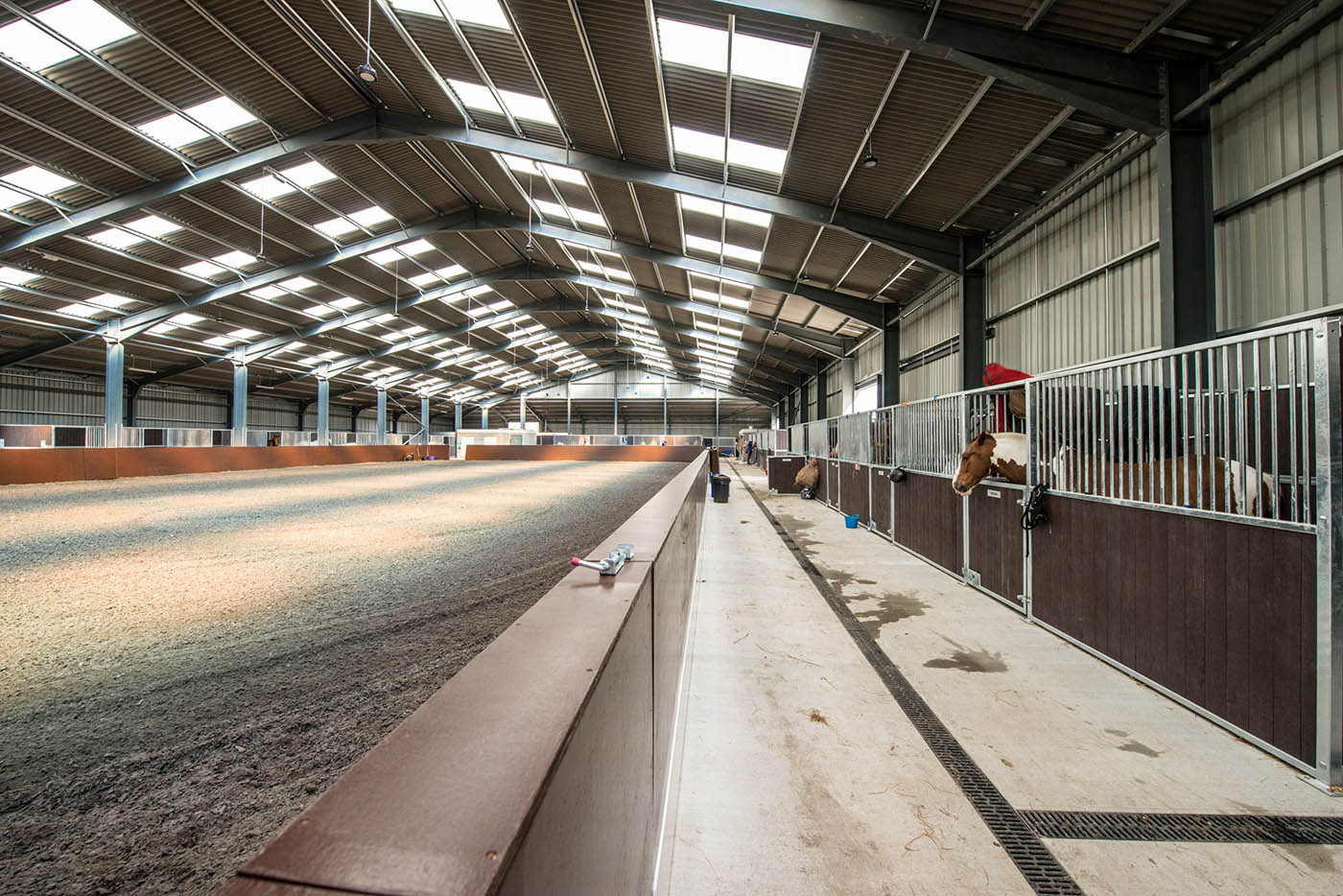 Indoor equestrian arena with sandy floor and horse stalls along the side