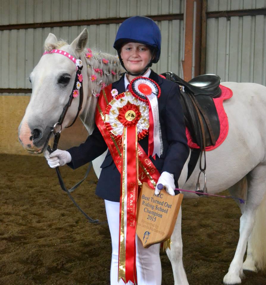 Person in equestrian attire holding ribbons next to a decorated white horse