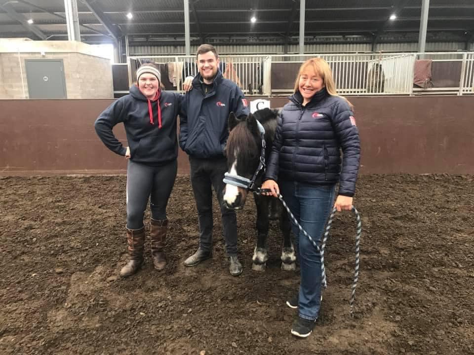 Three individuals with a pony inside an equestrian arena